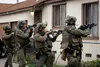 Armed federal officers in tactical gear advance along a residential street in Los Angeles during an ICE operation