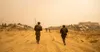 Three Israeli soldiers walking along a sand track between flattened buildings in Gaza