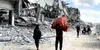 Palestinians walk past destroyed buildings in Gaza City carrying belongings