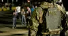An armed ICE officer in a vest marked Police ICE faces protesters at night outside the Delaney Hall detention centre in Newark