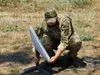 A Ukrainian soldier in camouflage kneels to set up a Starlink satellite dish in a dry field