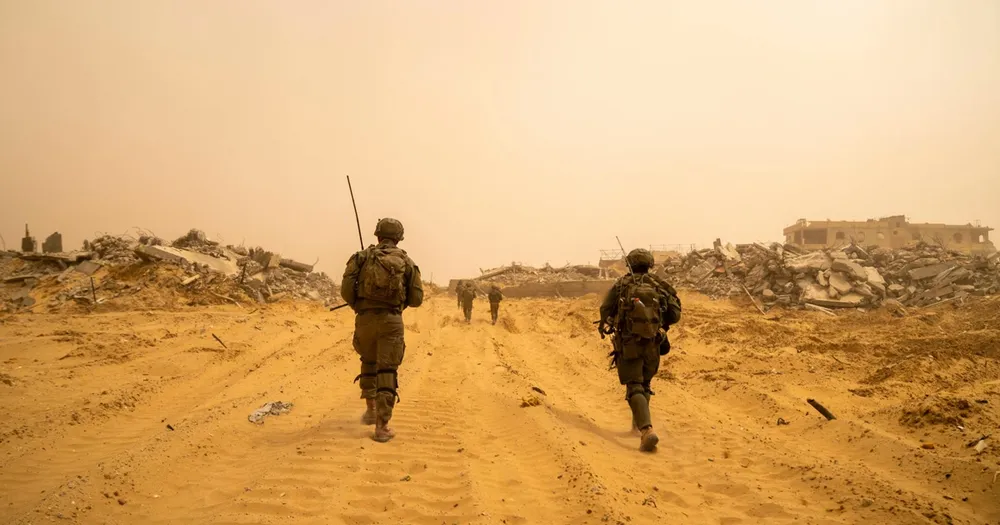Three Israeli soldiers walking along a sand track between flattened buildings in Gaza