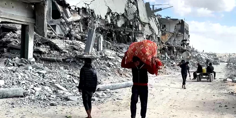Palestinians walk past destroyed buildings in Gaza City carrying belongings