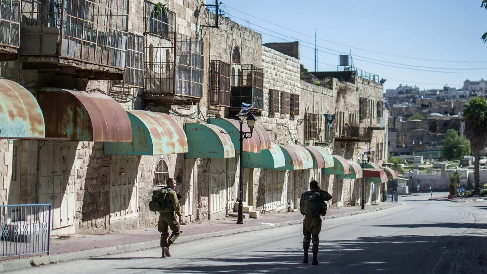 Two Israeli soldiers patrol past shuttered Palestinian shops on Shuhada Street in Hebron