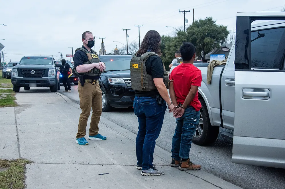 ICE ERO and HSI officers stand beside a handcuffed man at a roadside stop in San Antonio
