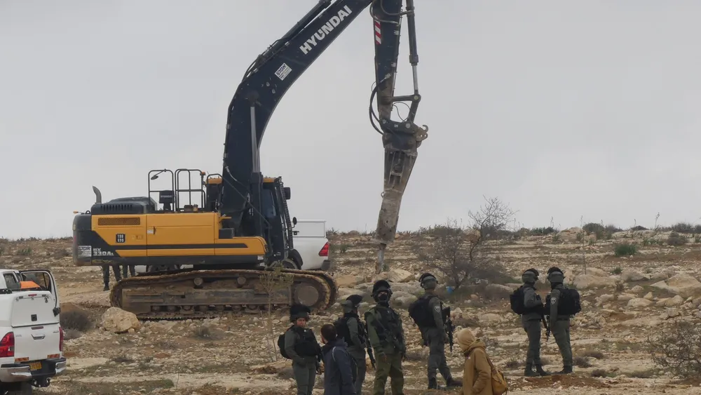 Israeli forces stand by an excavator demolishing Palestinian homes