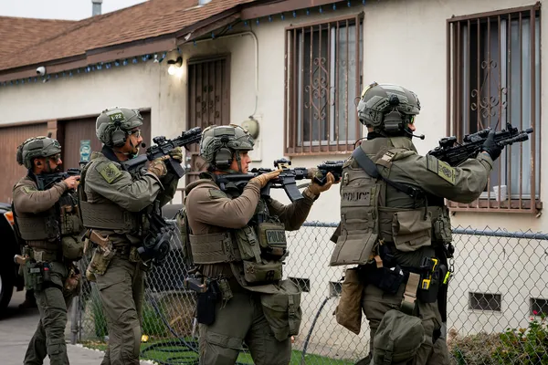Armed federal officers in tactical gear advance along a residential street in Los Angeles during an ICE operation