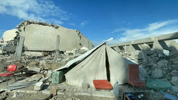 A canvas tent with a red cushion at its door, pitched among the concrete rubble of a bombed building in Gaza
