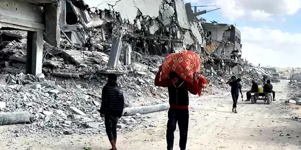 Palestinians walk past destroyed buildings in Gaza City carrying belongings