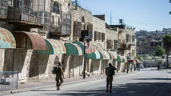 Two Israeli soldiers patrol past shuttered Palestinian shops on Shuhada Street in Hebron
