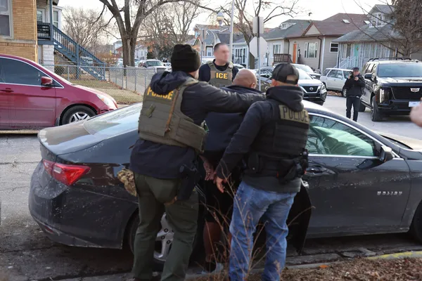 Two ICE officers in POLICE vests handcuff a man against a car during a vehicle stop in Chicago in January 2025