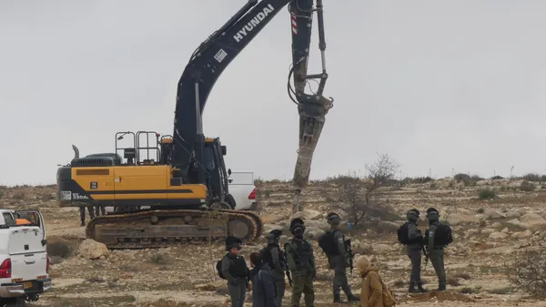 Israeli forces stand by an excavator demolishing Palestinian homes