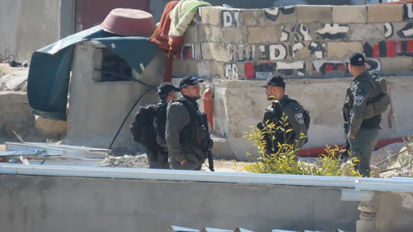 Four armed Israeli officers standing between Palestinian homes in Khallet Athaba